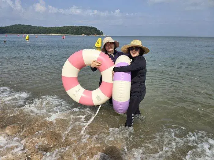 Two travelers with pool floats smiling at the seashore in Korea